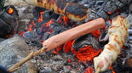 Pølser som stekes over bålet. To pølser innbakt i pinnebrød.