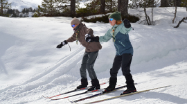 To speidere som står på ski ned en bakke mens de holder hender.